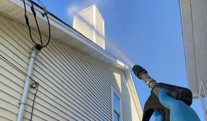 Soft washing a house exterior with a low-pressure spray